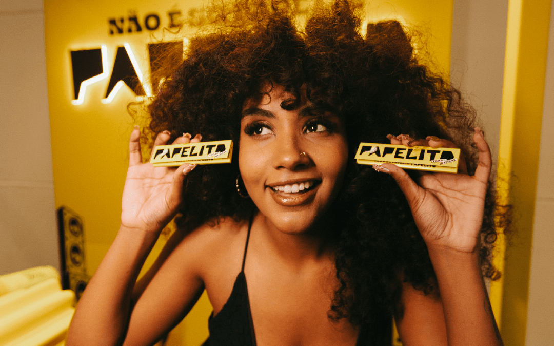 Mulher sorrindo e segurando papéis Papelito diante de um fundo amarelo.